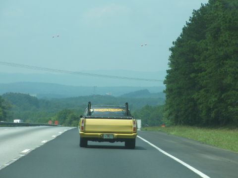 1972 Ford Ranchero - A yellow pickup truck with prominent dual exhaust pipes is seen from behind on a highway.