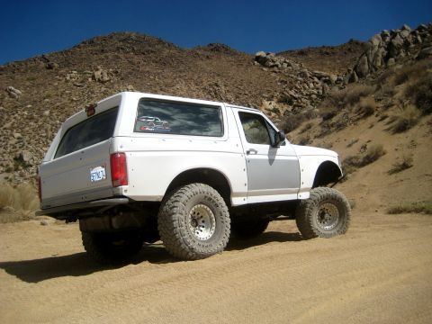 1996 Ford Bronco - This modified SUV is shown on a dusty trail with rocky hills under a clear blue sky.