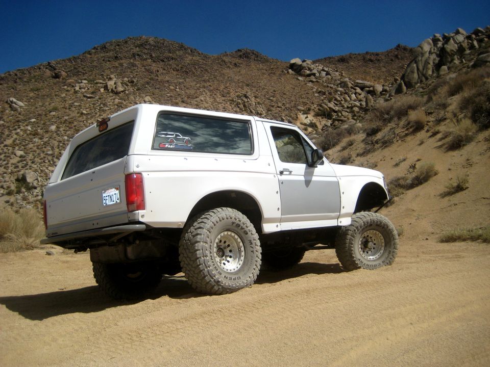 White SUV with large tires on a dirt road, mountains in background. License plate reads 6FTNL74