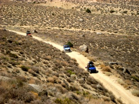 1996 Ford Bronco - Multiple off-road vehicles navigate a winding dirt path in a desolate, arid landscape.