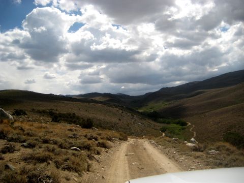1996 Ford Bronco - A dirt road leads through a barren valley with green vegetation in the distance, under a dramatic sky.