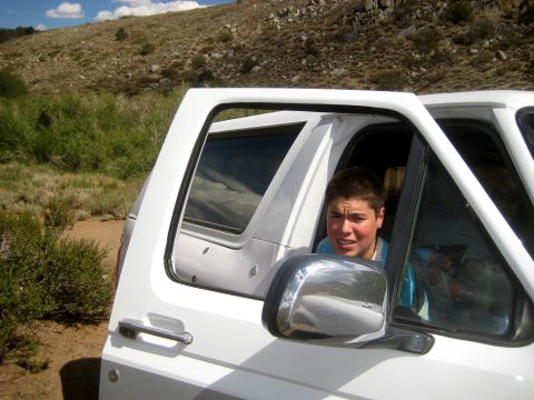 1996 Ford Bronco - A young man looks out the window of a white 1996 Ford Bronco parked in a dry, grassy area.