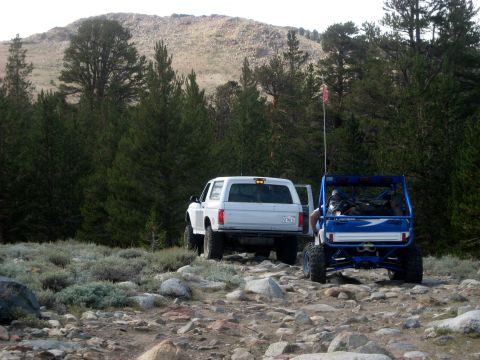 1996 Ford Bronco - Two off-road vehicles, a white 1996 Ford Bronco and a blue ATV, navigate a rocky mountain trail.