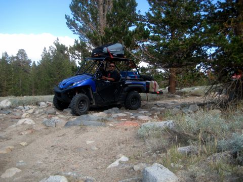1996 Ford Bronco - Blue side-by-side ATV navigates a rough, rocky trail through a wooded mountain area.