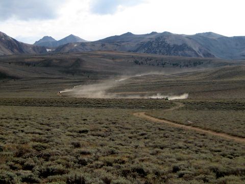 1996 Ford Bronco - Off-road vehicles traverse a dusty trail in a wide, mountainous landscape.