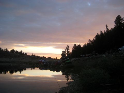 1996 Ford Bronco - A campsite is set up by a lake, with tents and vehicles visible as the sun sets over the horizon.