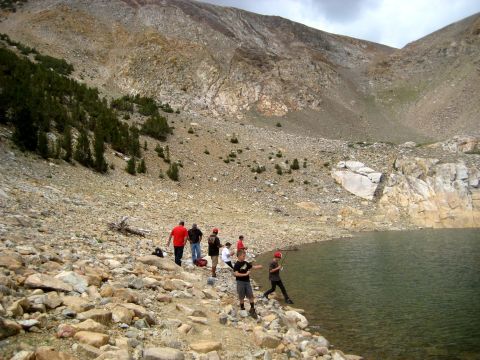 1996 Ford Bronco - Several people gather by the edge of a clear lake, with a steep, rocky mountainside dominating the background.
