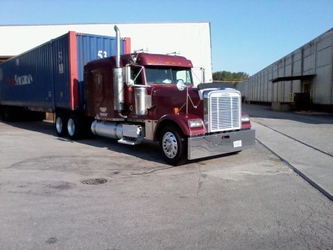 2003 Ford Crown Victoria - A maroon semi-truck is parked next to a blue shipping container in an industrial area.