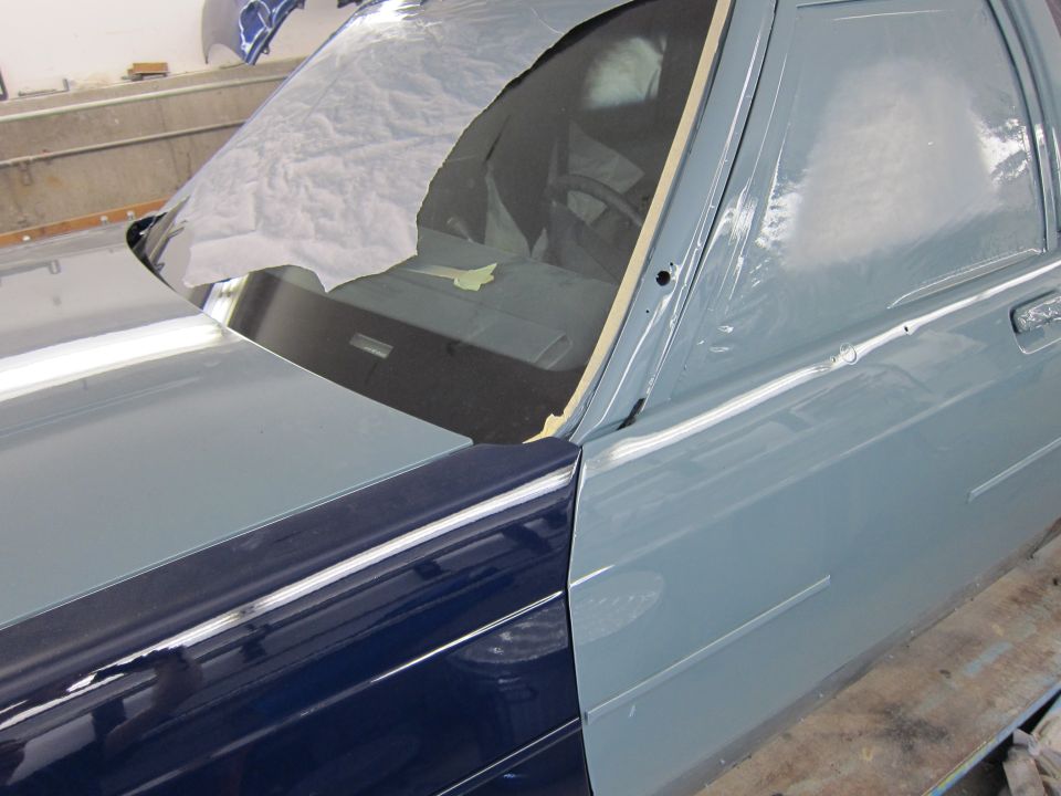 Ford Crown Victoria with blue and gray paint, partially covered in plastic wrap. The car is in a workshop