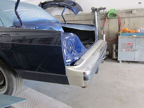 1991 Ford LTD Crown Victoria - A car is in a body shop with its trunk open, undergoing repairs or painting.