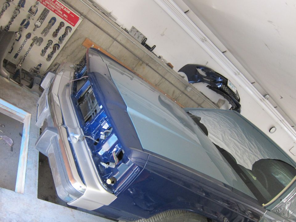 Blue car interior with exposed dashboard and front clip. Parts chart on wall