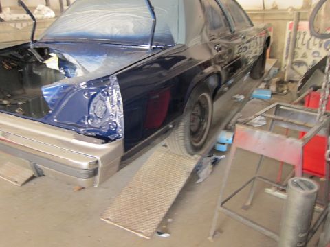 1991 Ford LTD Crown Victoria - A dark blue sedan is seen from the rear on a lift in a garage, with its trunk open and parts covered in plastic.