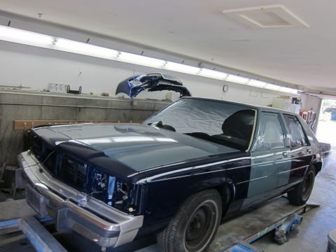 1991 Ford LTD Crown Victoria - A sedan, possibly a Ford Crown Victoria, is in a garage with its front end disassembled and parts of the body covered in tape and plastic.