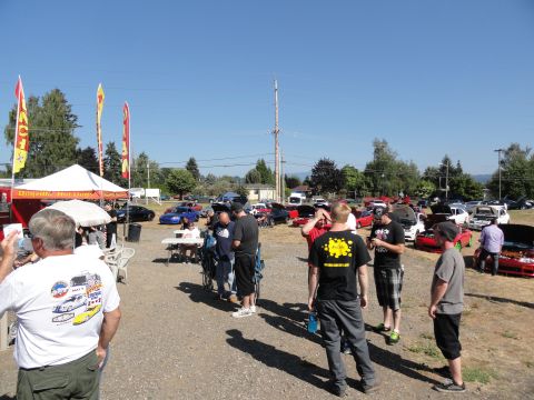 1964 Ford Fairlane - Attendees mingle at an outdoor car show, with tents and various vehicles visible in the background.