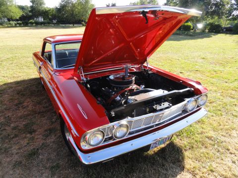 1964 Ford Fairlane - A bright red 1964 Ford Fairlane is parked on grass with its hood raised, revealing the engine bay.