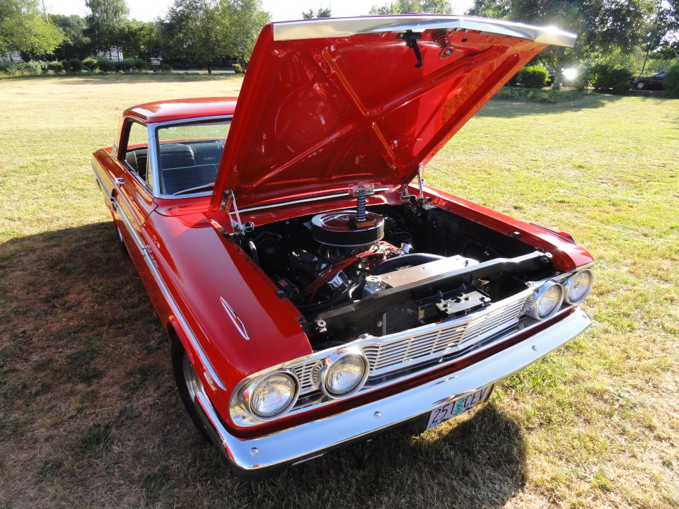 Red 1964 Ford Fairlane with hood open, showing engine. Chrome grille and bumper