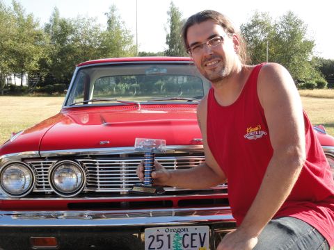 1964 Ford Fairlane - Man with trophy poses with a red 1964 Ford Fairlane, showing its distinctive grille and headlights.