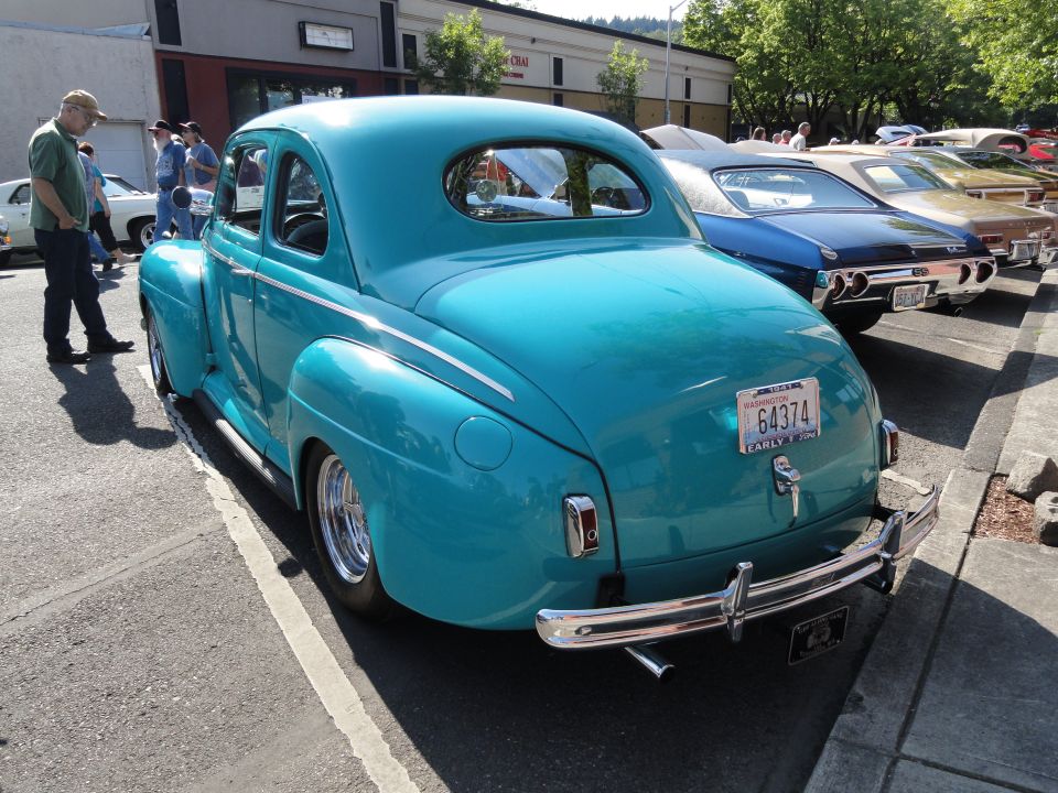 Teal coupe with chrome bumper and dual exhaust pipes, parked on asphalt