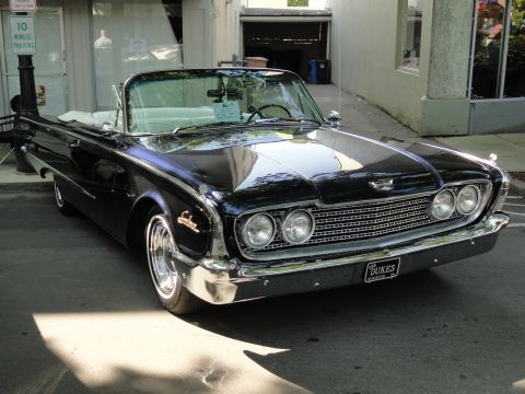 1964 Ford Fairlane - A black 1960 Ford Starliner convertible with a white top is parked on a street. The car has a prominent chrome grille and dual headlights.