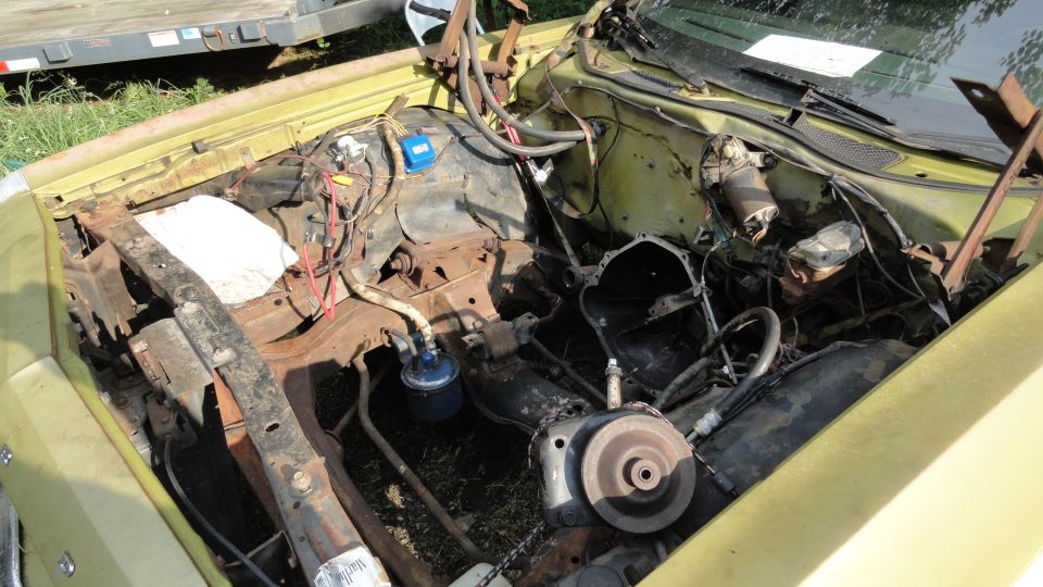 Yellow 1973 Ford Torino engine bay with disassembled engine components and visible rust