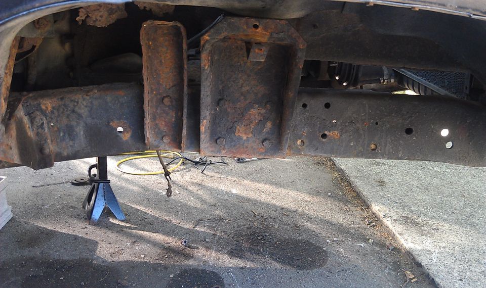 Rusty truck frame crossmember and floor pan supported on a jack stand