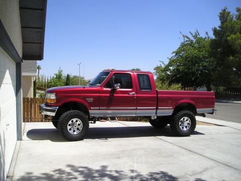 1997 Ford F-250 - A red 1997 Ford F-250 pickup truck is shown from the side, lifted with large tires.