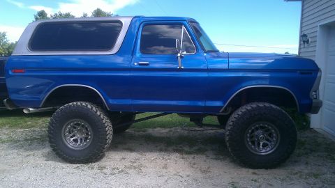 1978 Ford Bronco - A lifted 1978 Ford Bronco with large off-road tires sits parked outside a residential garage.