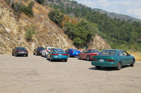 1993 Ford Taurus - A collection of vehicles are parked in a lot on a hillside, with a backdrop of trees and a mountain.