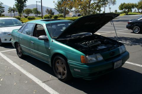1993 Ford Taurus - A green sedan is parked in a lot with its hood open, revealing the engine compartment.