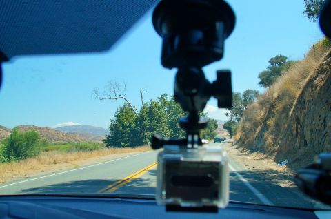 1993 Ford Taurus - A GoPro camera is mounted on the windshield, capturing the view of a road winding through a dry, hilly terrain under a clear blue sky.