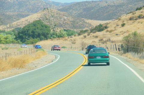1993 Ford Taurus - Multiple vehicles travel on a two-lane road through a dry, hilly landscape under a clear sky.