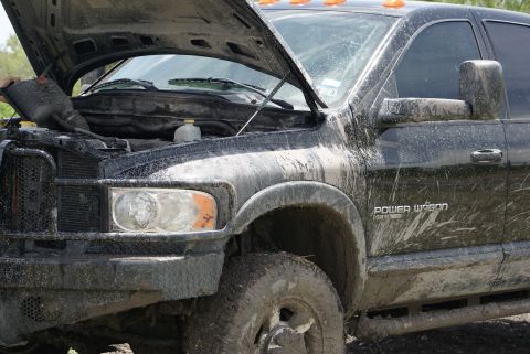 1989 Ford Bronco - Mud-covered black Dodge Power Wagon with its hood open, showing the engine compartment.