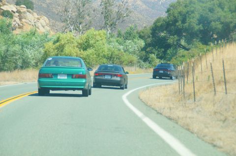 1993 Ford Taurus - Multiple vehicles travel down a rural highway on a sunny day.