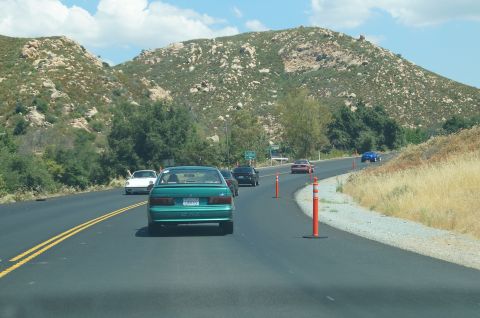 1993 Ford Taurus - Several cars drive along a highway with hills and dry grass on the sides under a partly cloudy sky.