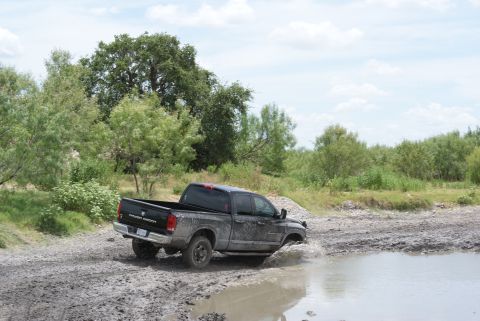 1989 Ford Bronco - A black pickup truck navigates a muddy terrain with water splashing.