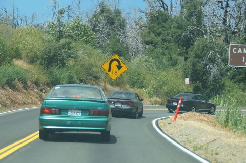 1993 Ford Taurus - A green 1993 Ford Taurus sedan is seen from the rear on a winding road, with other vehicles ahead.