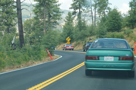 1993 Ford Taurus - A green 1993 Ford Taurus drives on a winding road, with other vehicles visible ahead.