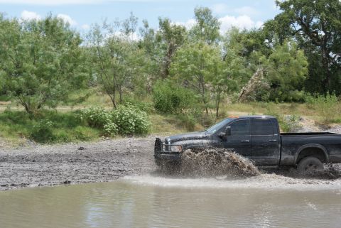 1989 Ford Bronco - Pickup truck navigates through water, kicking up a large spray.