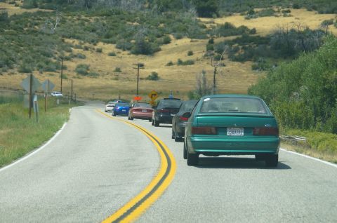 1993 Ford Taurus - A line of cars travels down a rural highway, led by a green sedan.