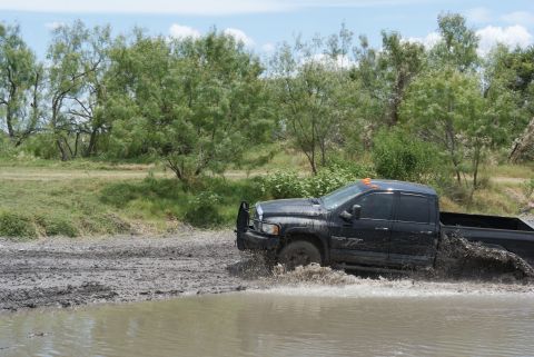 1989 Ford Bronco - A black pickup truck navigates a muddy terrain, kicking up water and mud as it drives.