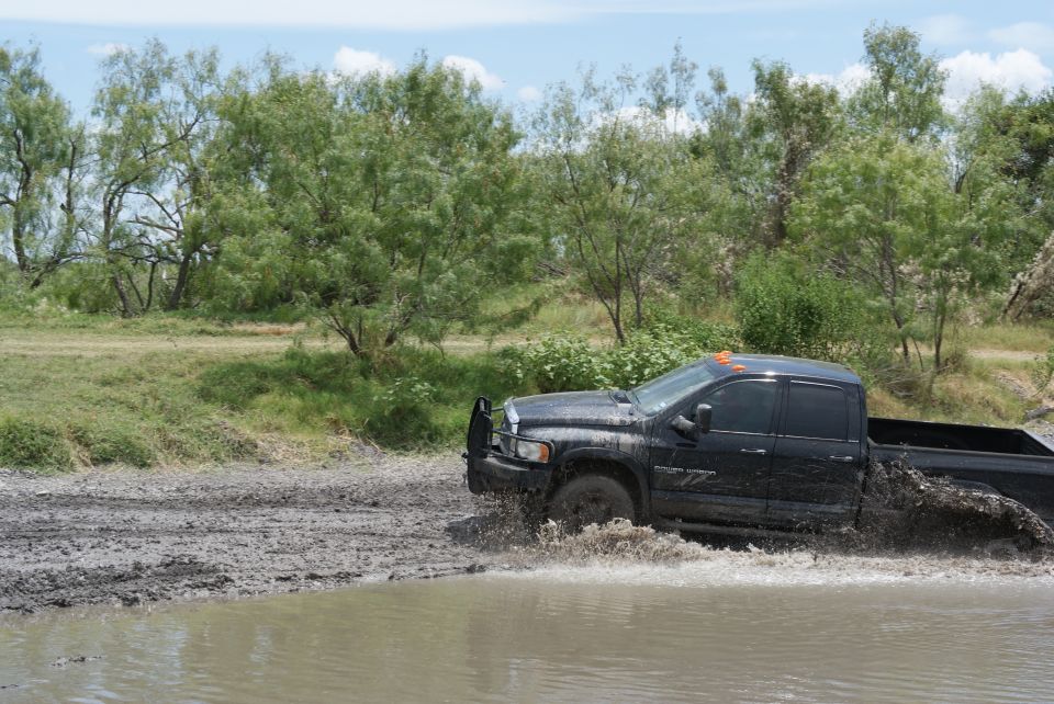 Black pickup truck splashing through mud, side view