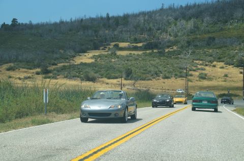 1993 Ford Taurus - Multiple vehicles travel down a road through a landscape with dry vegetation and hills.