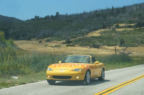 1993 Ford Taurus - A yellow convertible with flame decals drives down a two-lane road through a dry, hilly landscape.