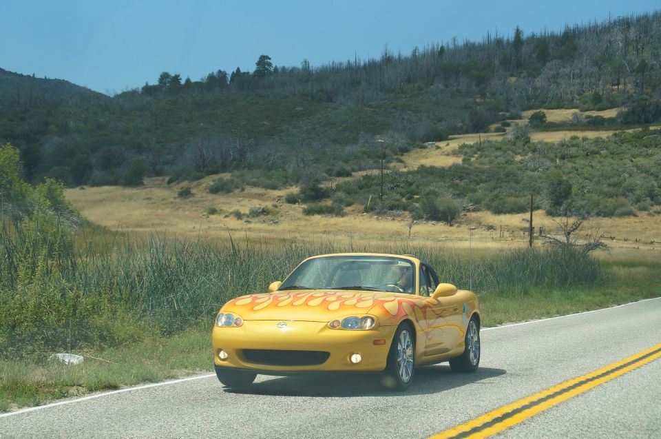 Yellow convertible with flame decals driving on a road with hills and dry grass in the background