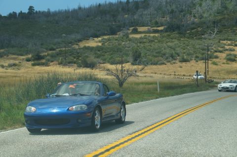 1993 Ford Taurus - A blue convertible sports car is seen driving on a road, with another white car visible further down the road.