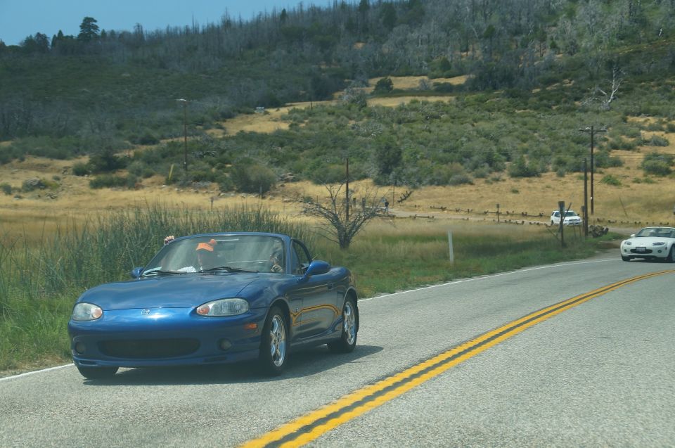 Blue convertible sports car driving on a road with a white car in the distance