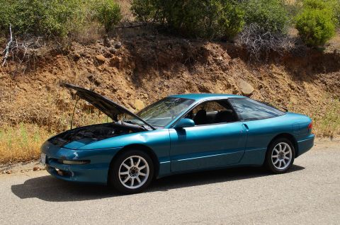 1993 Ford Taurus - A teal coupe sits on the shoulder of a road, its hood raised to reveal the engine bay.