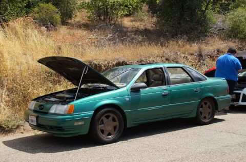 1993 Ford Taurus - A 1993 Ford Taurus sedan is parked on the side of a road with its hood open, with another vehicle and a person nearby.