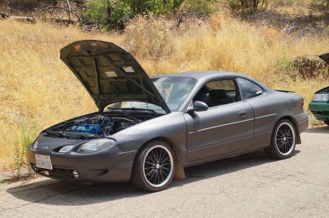 1993 Ford Taurus - A gray Ford Escort coupe is parked with its hood open, revealing the engine bay.