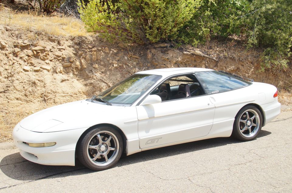 White Ford Probe GT parked on a dirt road with trees and rocks in the background